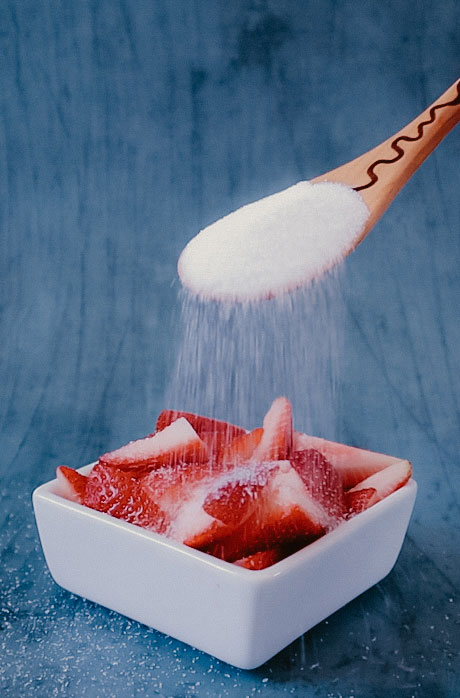 A wooden spoon pouring sugar over strawberries.