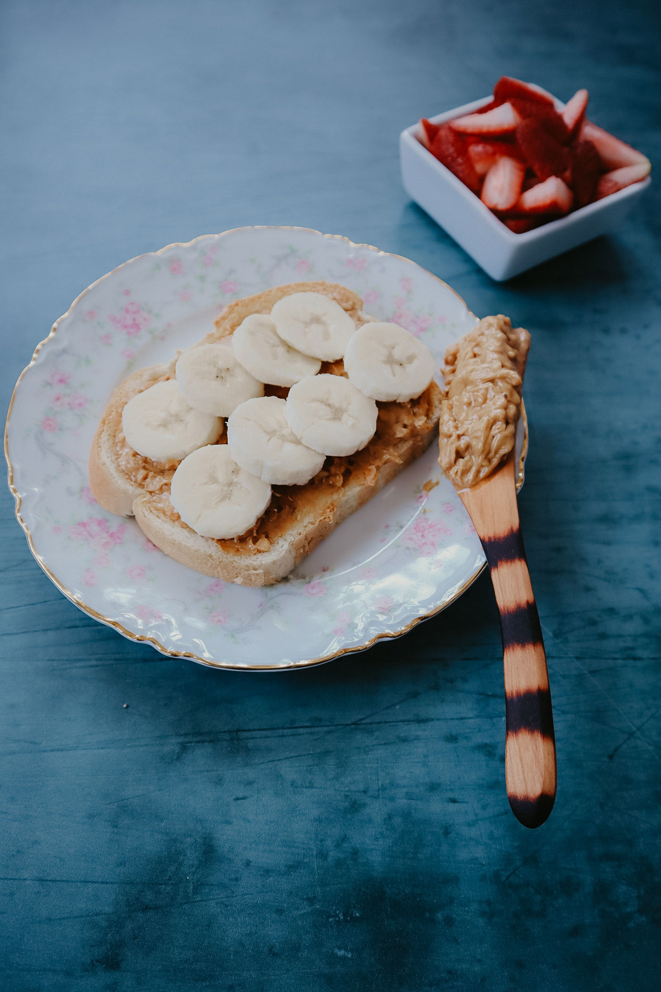 A wooden knife being used to spread peanut butter.
