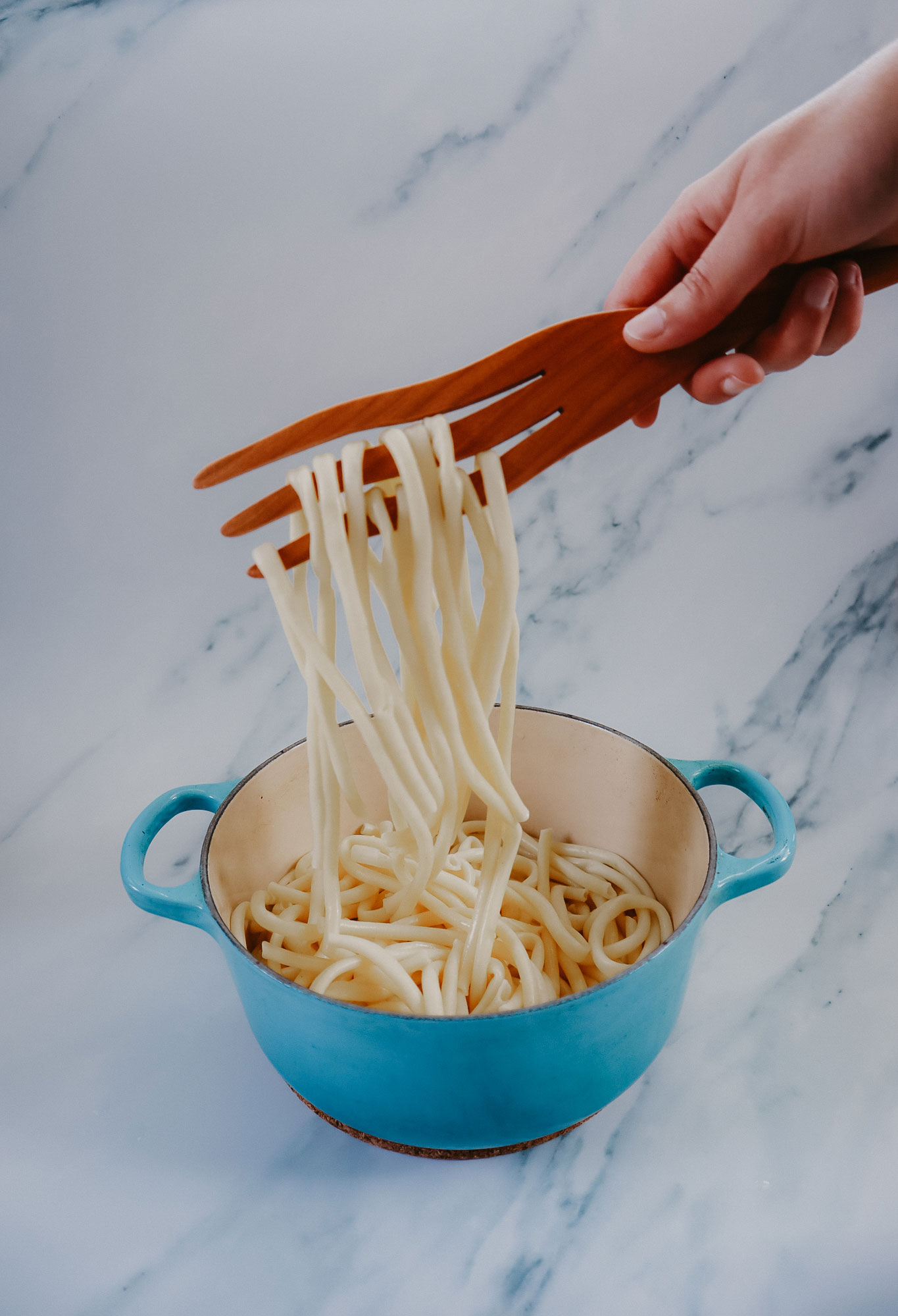 A wooden fork entangling noodles.