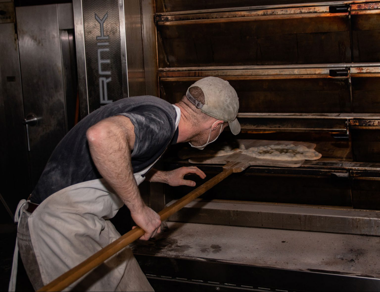 A baker placing pizzas in a large oven.