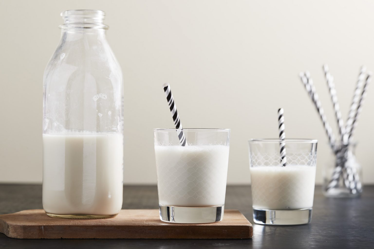 A glass jar of milk next to two to full glasses of milk.