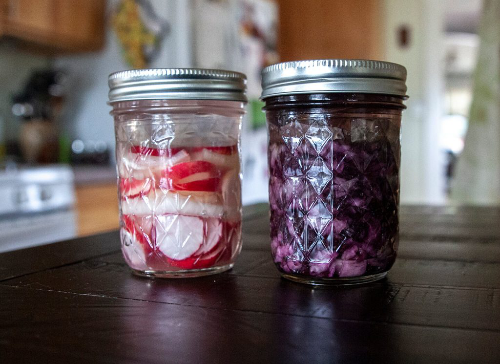 Two glass jars holding fermented radishes and red cabbage.