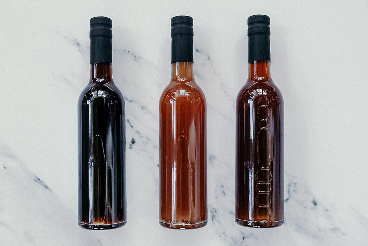 Three bottles of varying shades of brown holding vinegar.