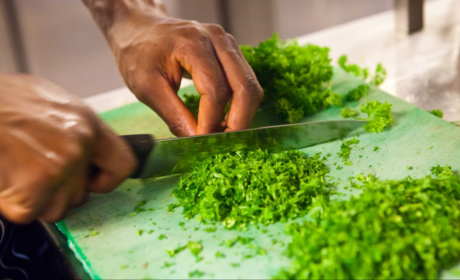 A person chopping herbs on a green cutting board.