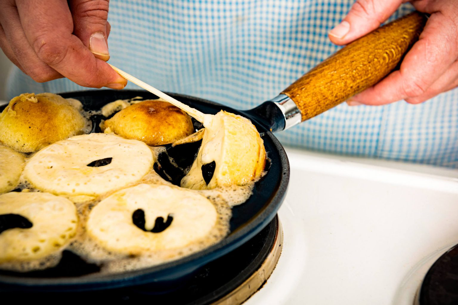 A person using an aebleskiver pan to make Danish pancake balls.