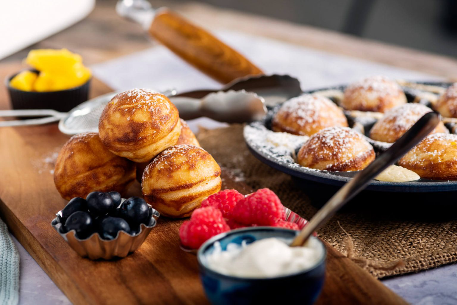 Danish pancake balls topped with powdered sugar and accompanied by a variety of fresh berries.