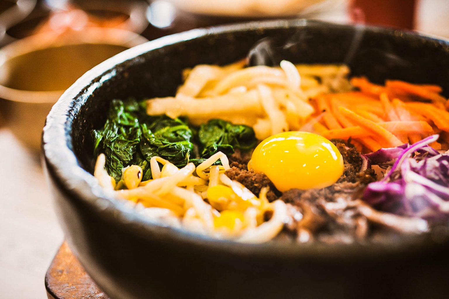 A dolsot bowl filled with bibimbap, a layer of rice topped with meats, veggies and an over-easy egg.