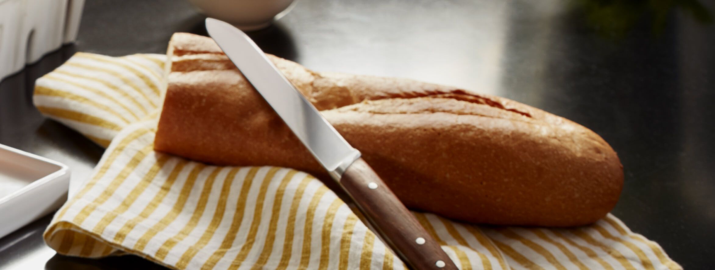 Loaf of crusty bread sitting on a yellow and white striped dish towel with a bread knife resting on top of bread.