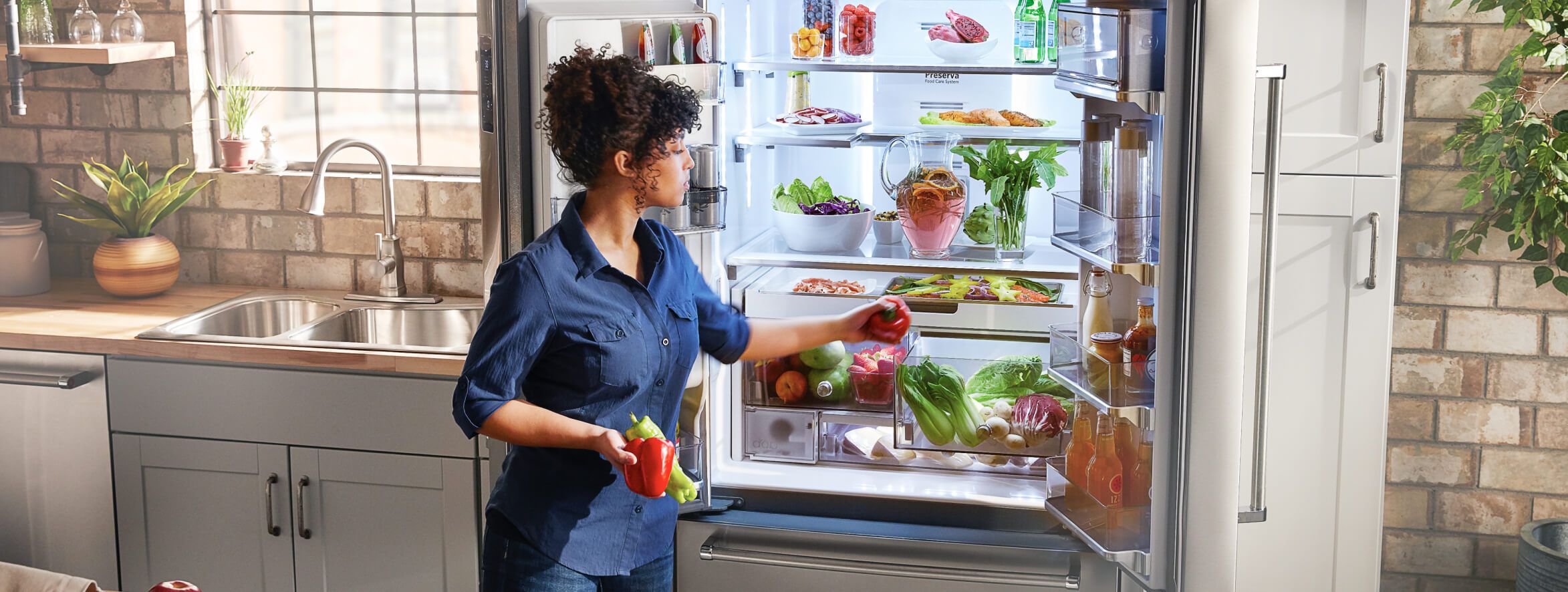 Woman selecting red and green peppers from a KitchenAid® French Door Refrigerator.