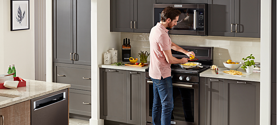 Man cooking on a KitchenAid® range in a kitchen with gray cabinetry.