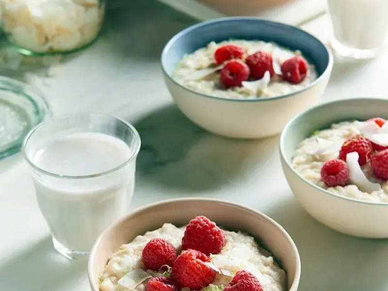 Bowls of lime coconut rice porridge with raspberries next to glass of milk 
