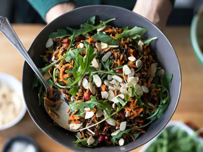 Person holding bowl of shredded carrot, arugula and wild rice salad 