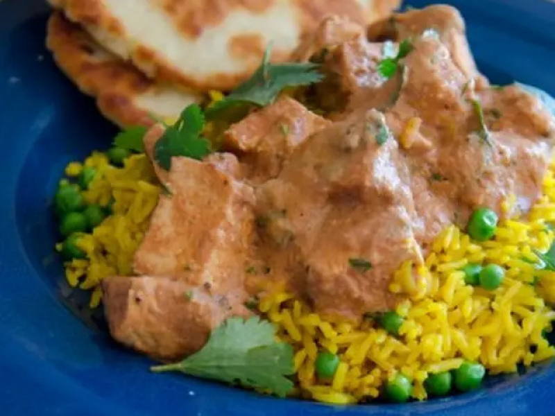 Close-up of chicken tikki masala on a bed of rice and peas