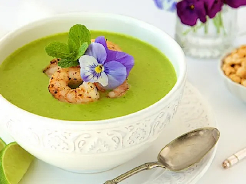 Bowl of asparagus and shrimp coconut curry garnished with purple flower 