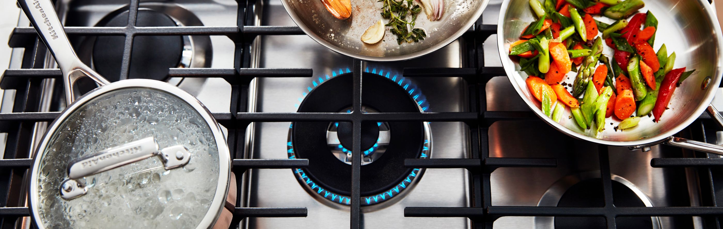 Gas stovetop with lit burner and several pots and pans sautéing food