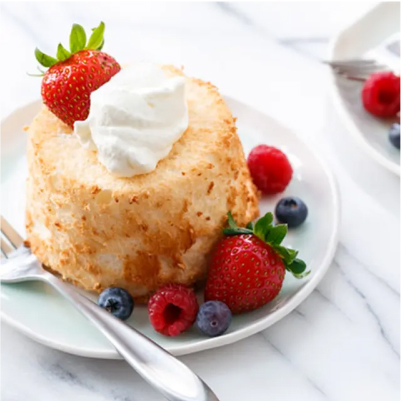 A mini angel food cake with whipped cream and berries.