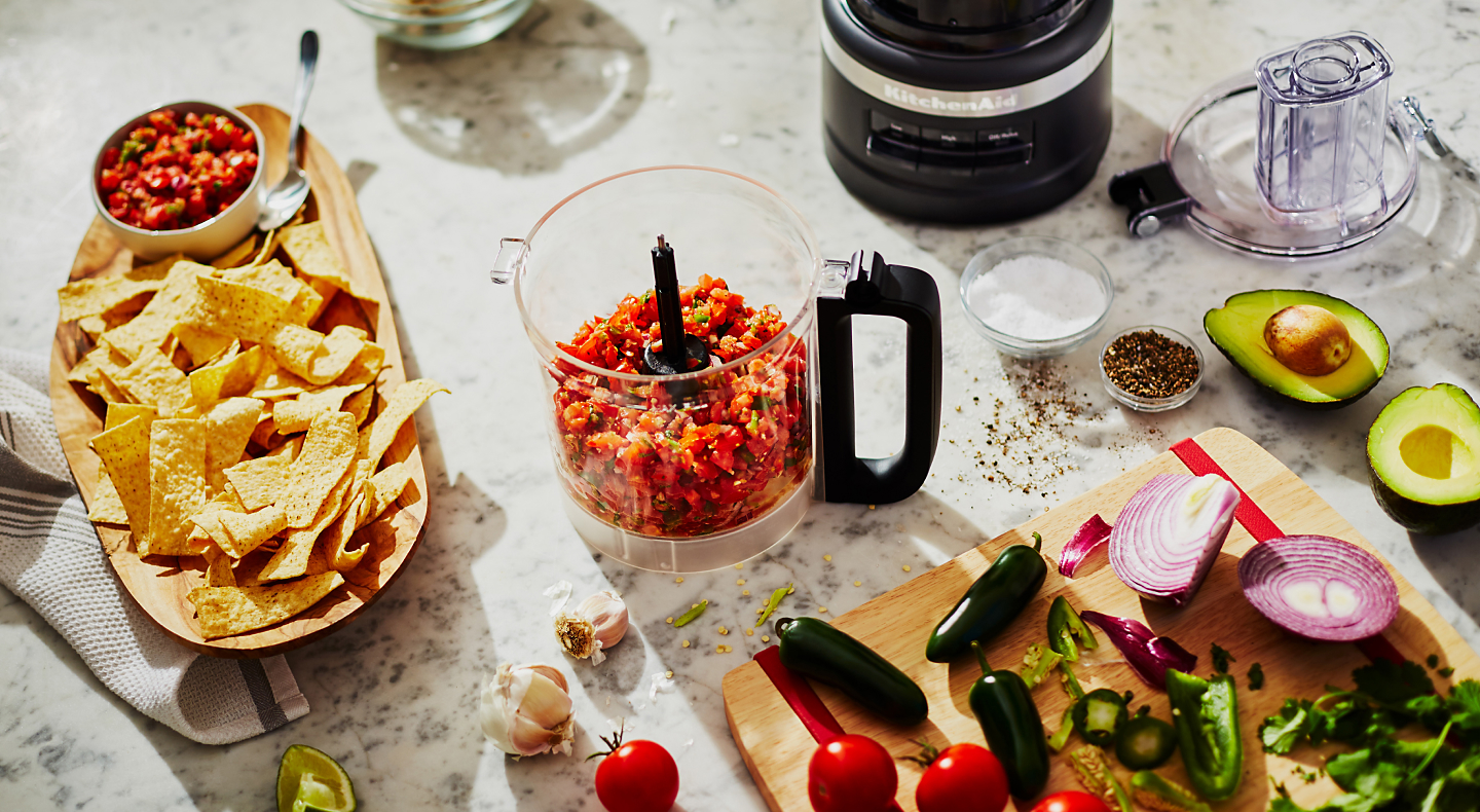 Fresh salsa in a food processor with ingredients around it on the counter