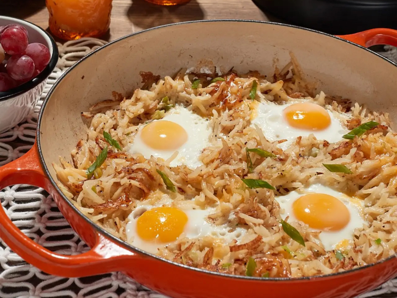 Potato hash with sunny side up eggs in red skillet