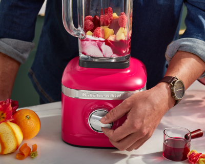 Person selecting settings on hibiscus KitchenAid® blender filled with fruit