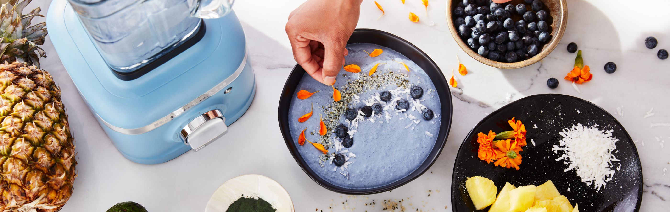Person garnishing a blue smoothie bowl next to blue KitchenAid® blender