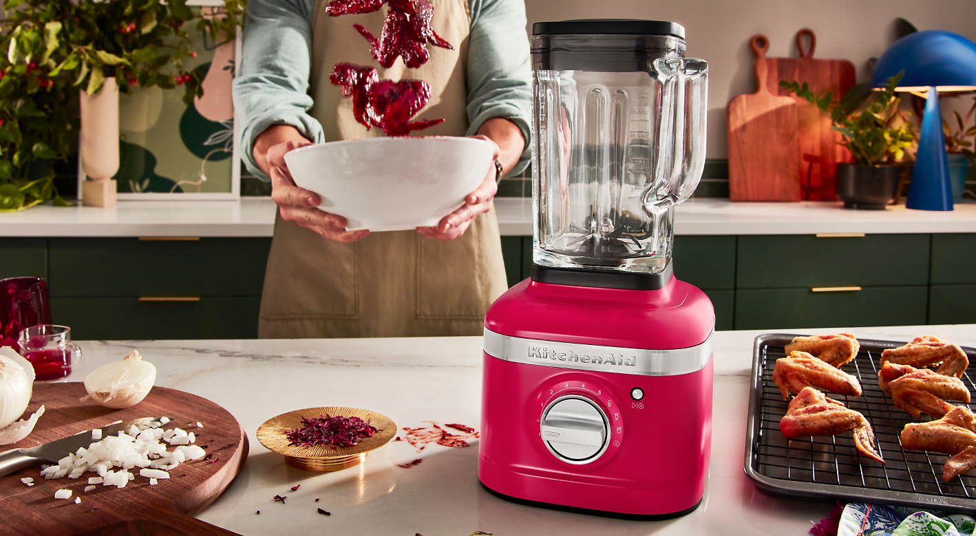  A person tossing hibiscus glazed wings with a Hibiscus Blender on the countertop. 