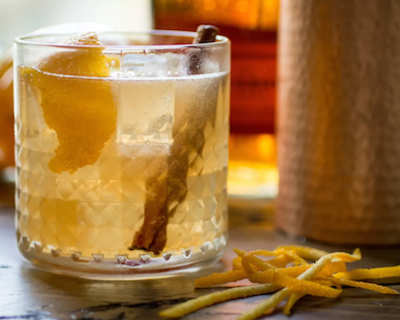 Glass of a bourbon old fashioned with a cinnamon stick and lemon wedge