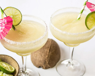 Two frozen coconut margaritas with lime wedges, straws and drink umbrellas