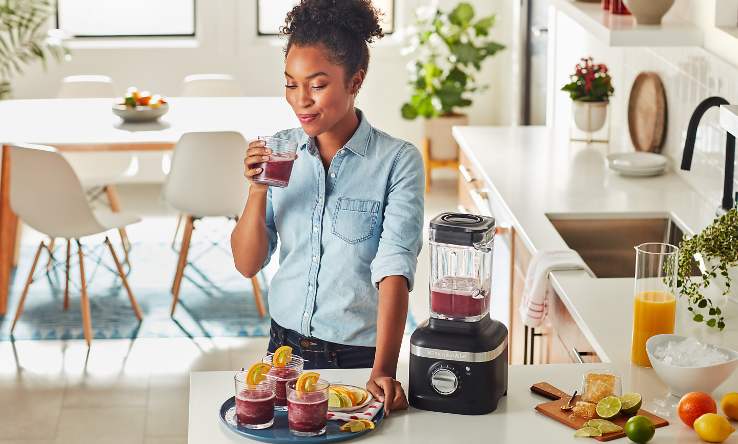 Woman drinking blended beverage next to black blender and serving tray