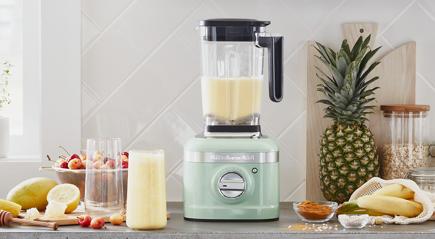 Mint green blender with with yellow slushie surrounded by ingredients