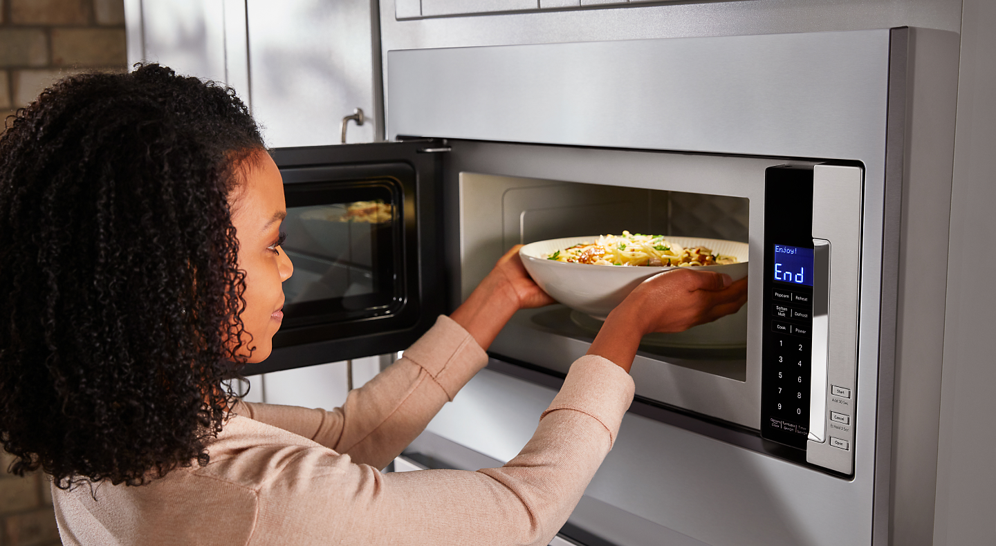 Woman placing a bowl inside built-in microwave