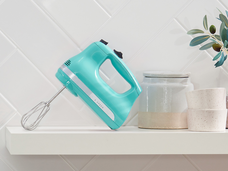 A teal KitchenAid® hand mixer on a modern kitchen counter.