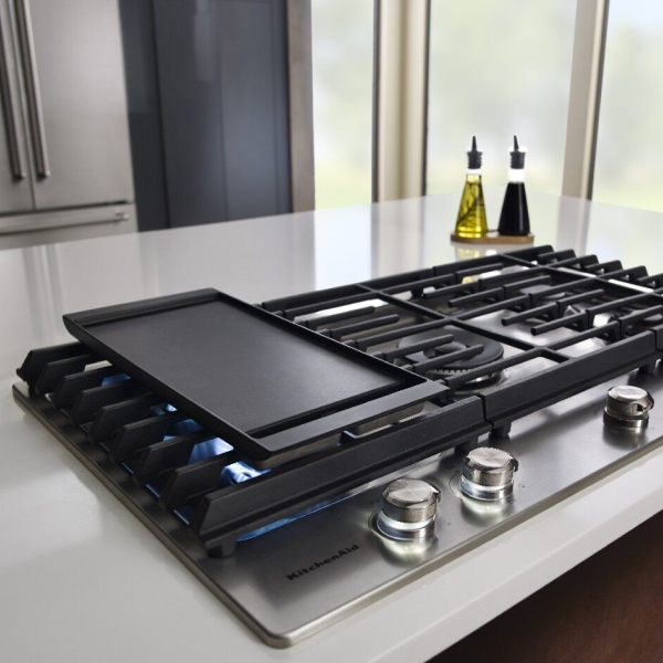 Griddle resting vertically on the left side of a gas cooktop
