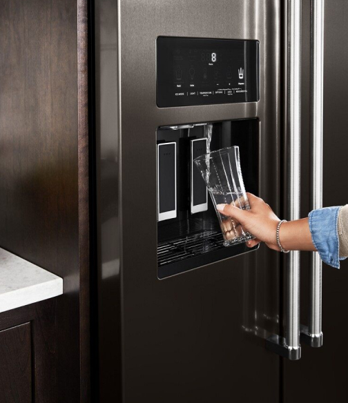 Person filling a glass from a refrigerator water dispenser