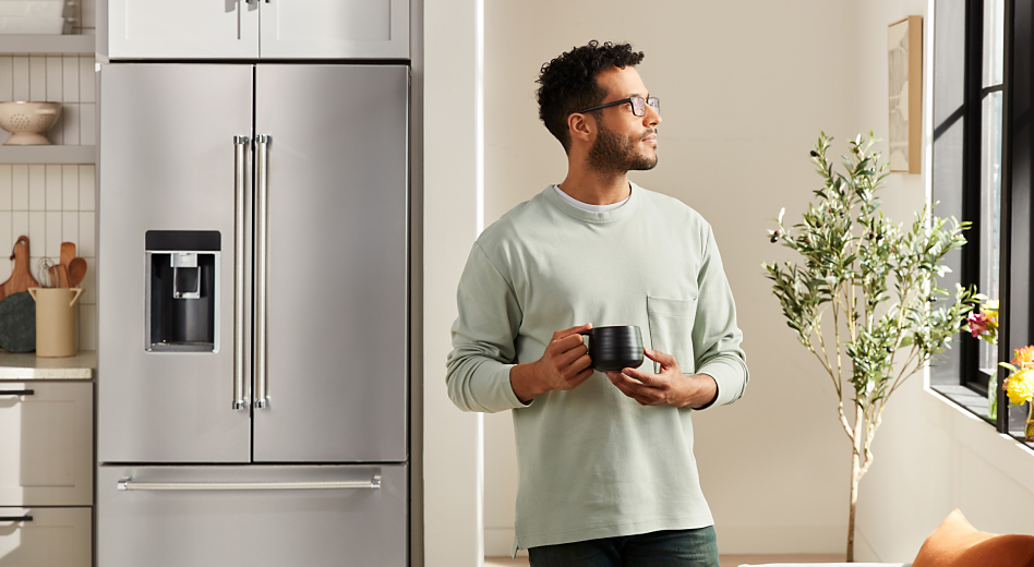 Person holding a mug next to a French door refrigerator