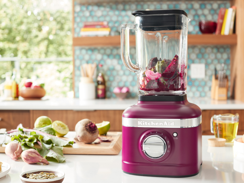 A KitchenAid® blender with fresh vegetables on a modern kitchen counter.