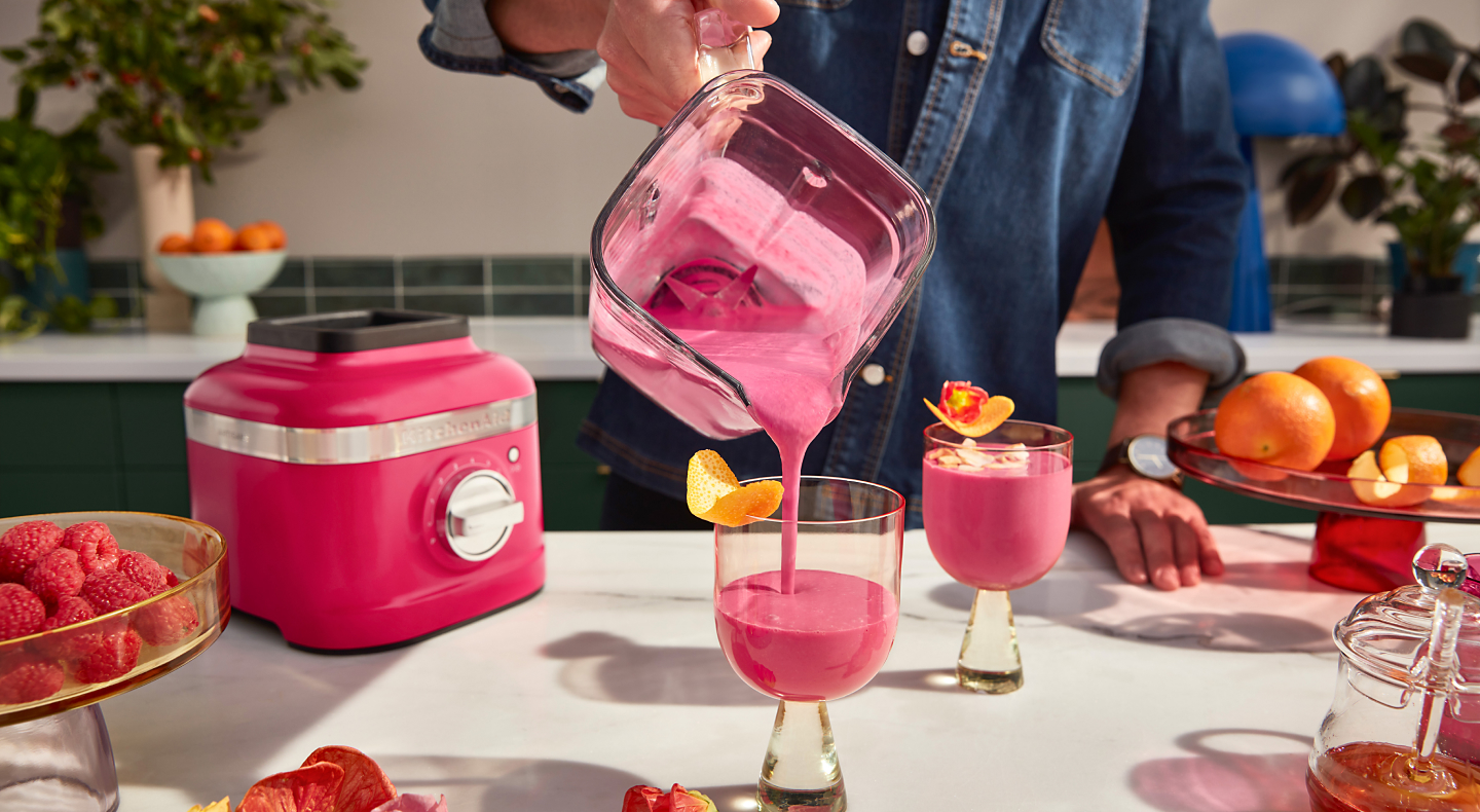  A man pouring a freshly made smoothie from a KitchenAid® blender pitcher into a glass.