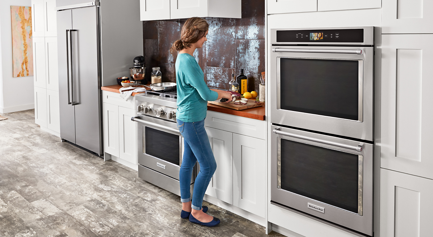 A woman chopping vegetables next to a KitchenAid® double wall oven