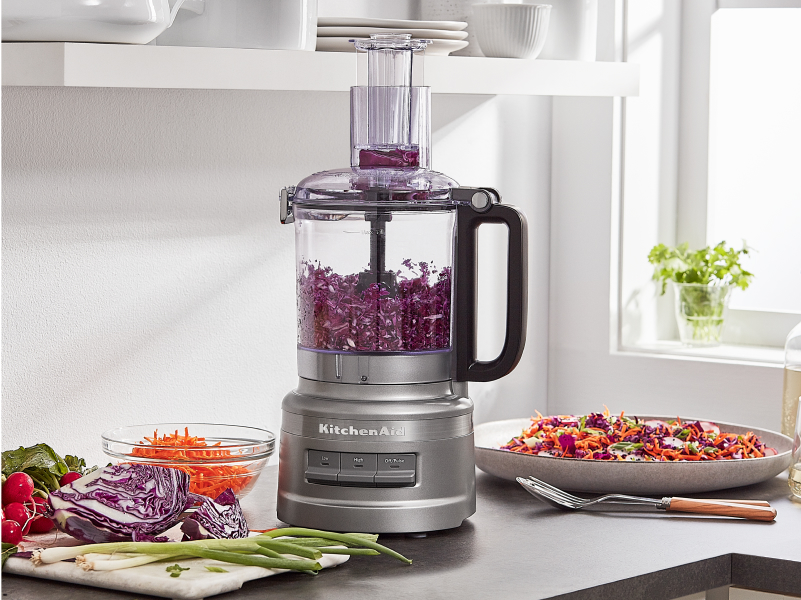 A KitchenAid® food processor with red onions inside.