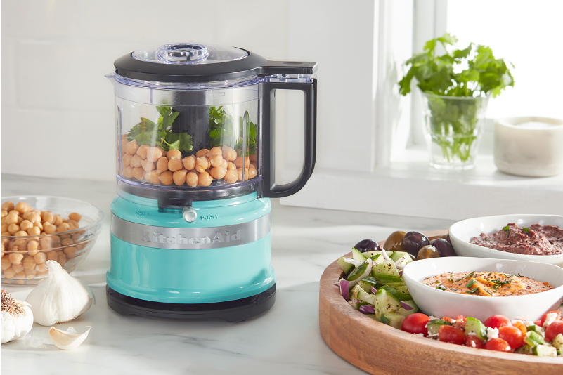 A KitchenAid® food processor next to veggies and hummus.
