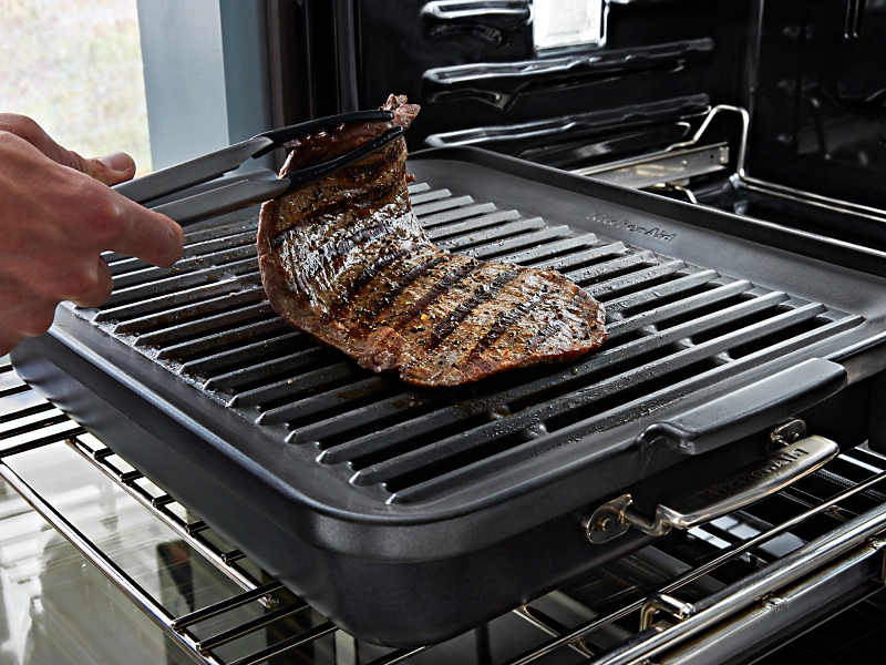 Maker using tongs to flip steak on Grilling Attachment in KitchenAid® Smart Oven+