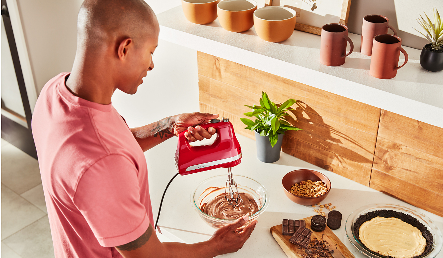 A man using a KitchenAid® hand mixer to make chocolate pie filling.
