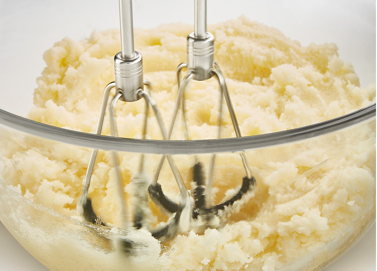 A closeup of KitchenAid® hand mixer beaters mashing potatoes.
