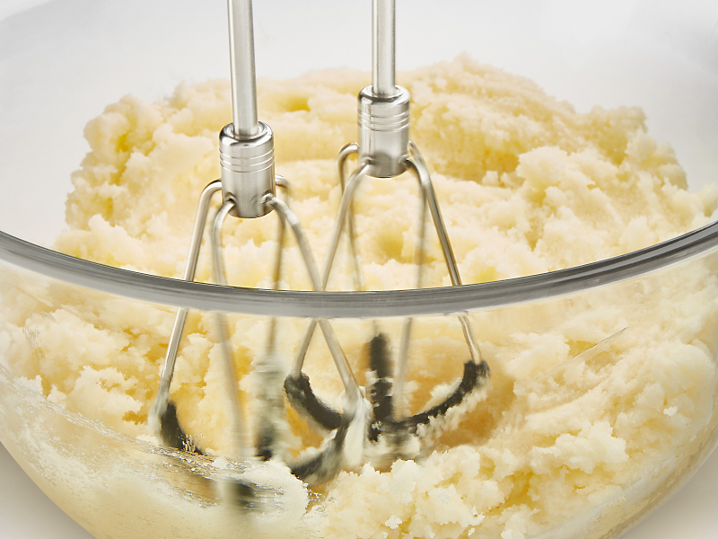 A closeup of KitchenAid® hand mixer beaters mashing potatoes.