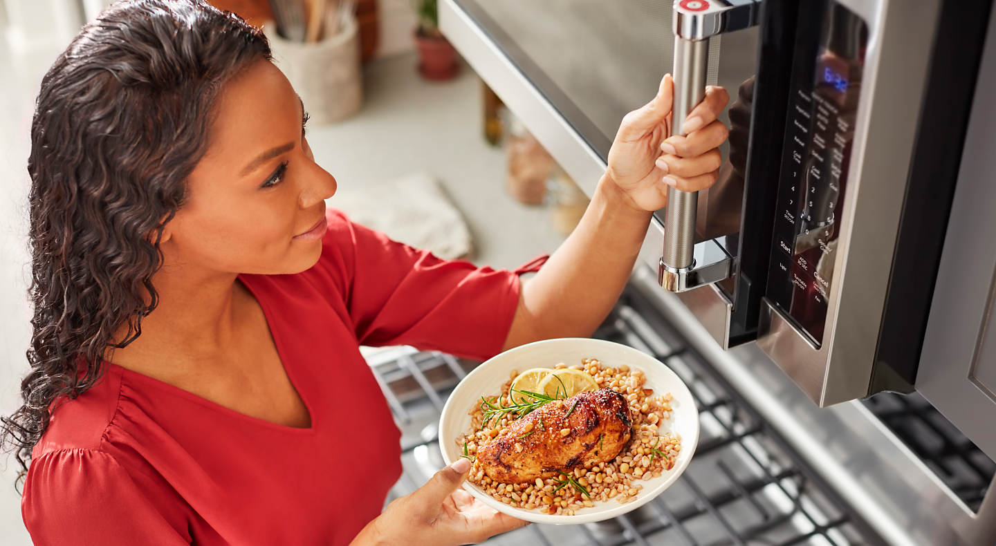 Person preparing heat up food in a KitchenAid® stainless steel microwave