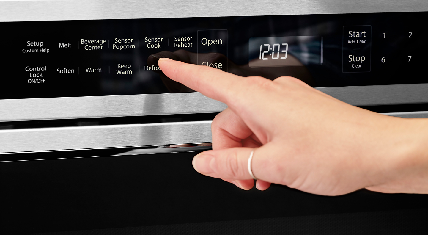 Person using the defrost option on a KitchenAid® microwave