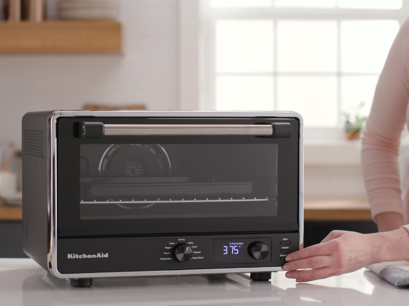 A woman programming a KitchenAid® countertop oven with air fry.