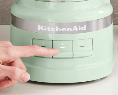 A person selecting a setting on a green KitchenAid® food processor