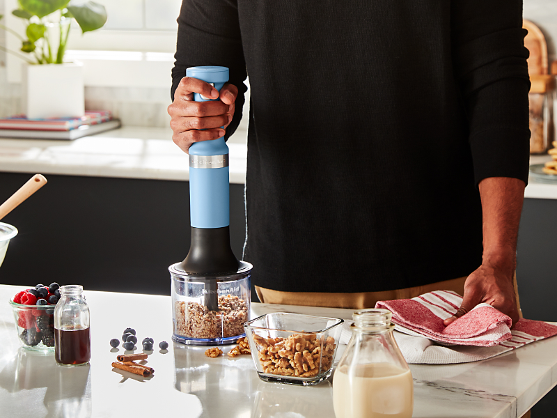 A person using a KitchenAid® immersion blender to process nuts
