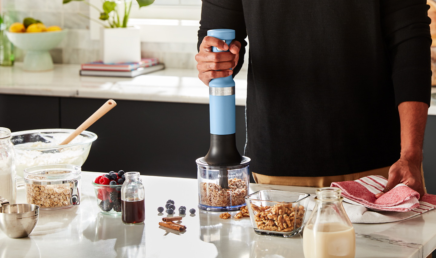 A person using a KitchenAid® immersion blender to process nuts