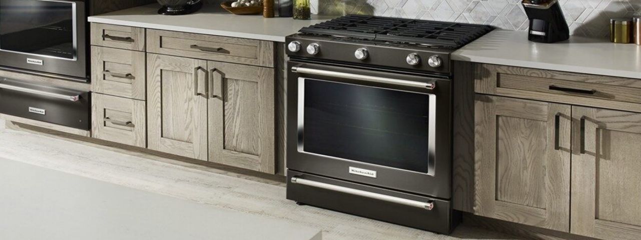 A black, self-cleaning oven installed in a clean, fully stocked kitchen.